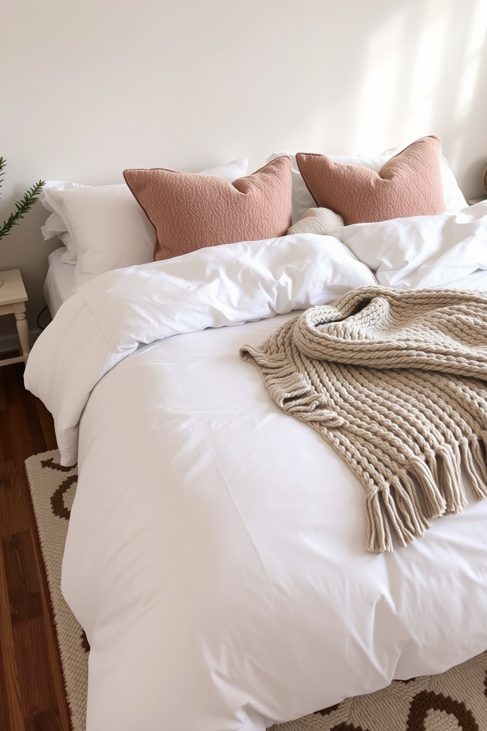 A cozy bedroom setting that embraces warmth and comfort. Soft layered textiles adorn the bed, featuring a plush duvet, decorative throw pillows, and a chunky knit blanket. The walls are painted in a soft neutral tone, creating a serene atmosphere. A stylish area rug lies beneath the bed, complementing the overall color scheme and adding an inviting touch.