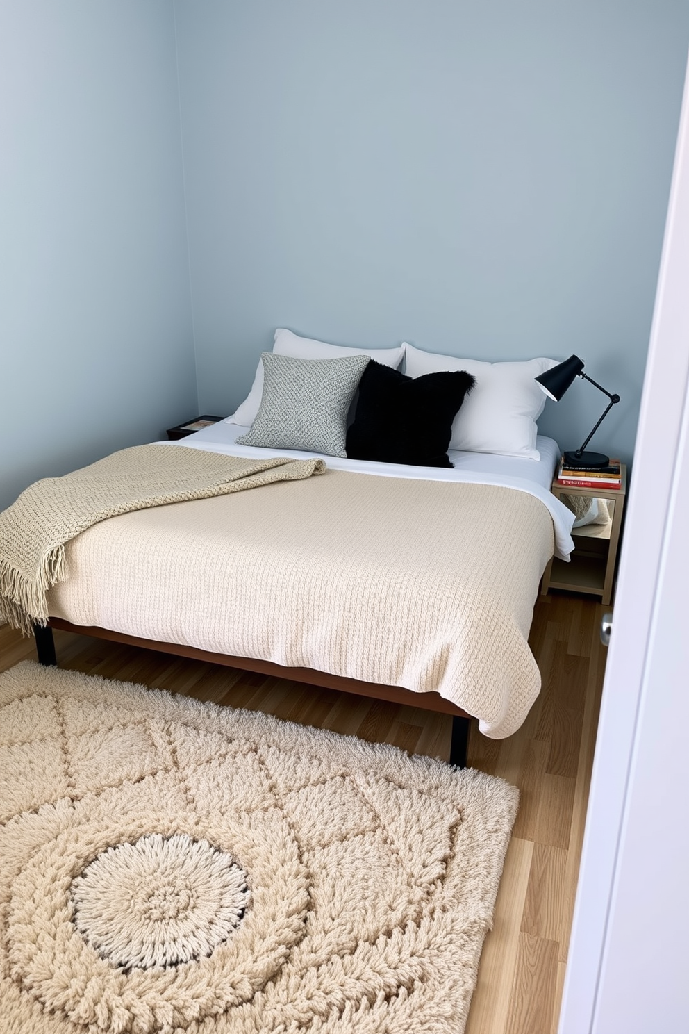 A cozy 10x10 bedroom featuring a soft area rug that defines the sleeping space. The bed is adorned with plush pillows and a textured throw blanket, creating an inviting atmosphere. Next to the bed, a small nightstand holds a stylish lamp and a stack of books. The walls are painted in a calming light blue, enhancing the serene vibe of the room.