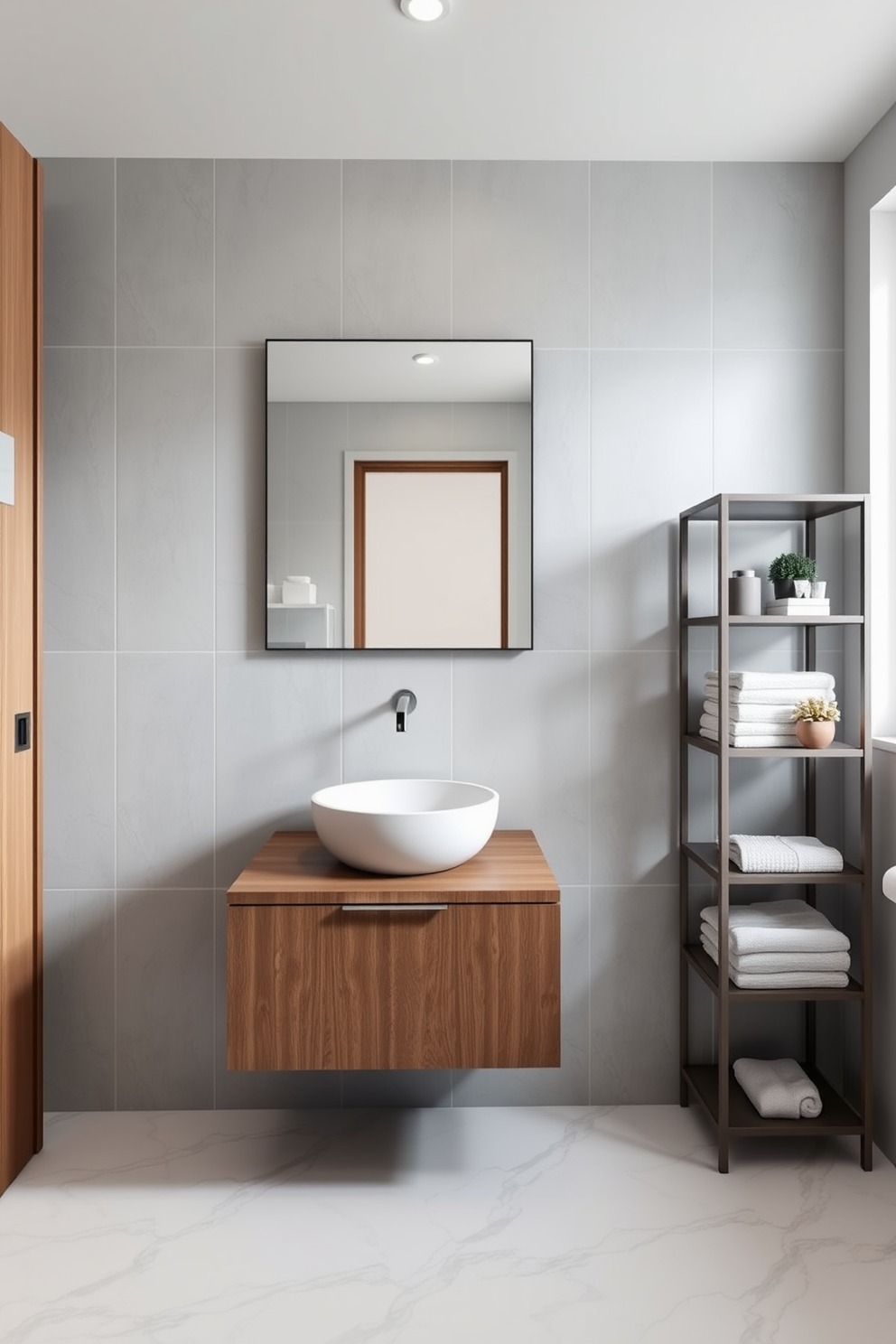 A stylish bathroom featuring a round sink integrated into a sleek wooden vanity. The walls are adorned with soft gray tiles, and the floor is finished with elegant marble, creating a harmonious and luxurious atmosphere. To the right of the sink, a minimalist shelving unit displays neatly folded towels and decorative items. A large frameless mirror reflects the natural light coming from a nearby window, enhancing the spacious feel of the 5x7 bathroom design.