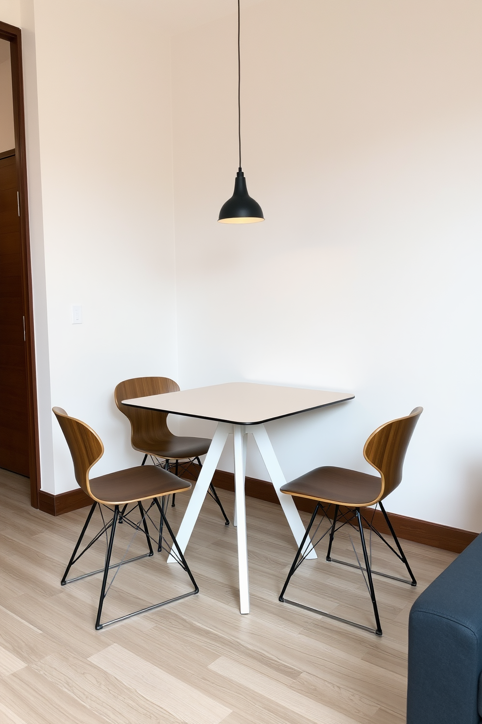 A compact dining table with sleek lines and a minimalist design is placed in the center of the space. Surrounding the table are four modern chairs with a mix of wood and metal finishes, creating a stylish yet functional dining area. The walls are painted in a neutral tone, enhancing the room's spacious feel. A small pendant light hangs above the table, adding a warm ambiance and making it the perfect spot for casual meals or entertaining guests.