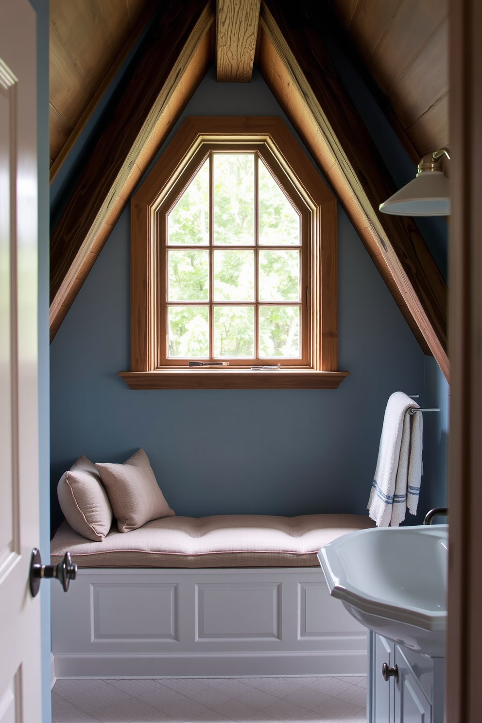 A charming attic bathroom with sloped ceilings and exposed wooden beams. The space features a freestanding clawfoot tub positioned beneath a small window, allowing natural light to flood in. Vintage fixtures add character, including an antique-style faucet and a pedestal sink with intricate detailing. The walls are painted in a soft cream color, complemented by a rustic wooden shelf displaying neatly rolled towels and decorative jars.