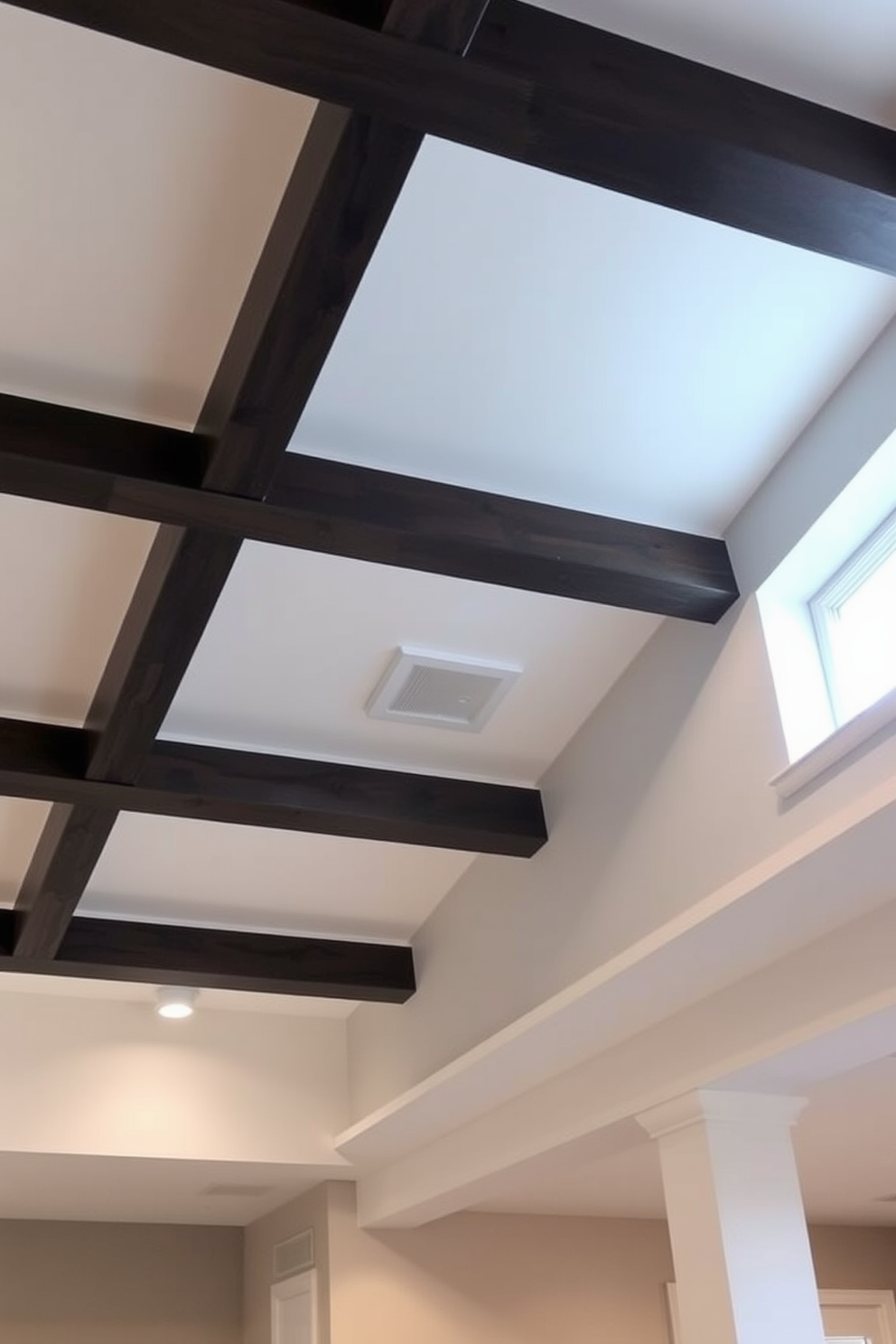 A modern basement ceiling design featuring soffits that cleverly conceal ductwork. The soffits are painted in a soft white, contrasting with the rich dark wood beams that add warmth to the space.