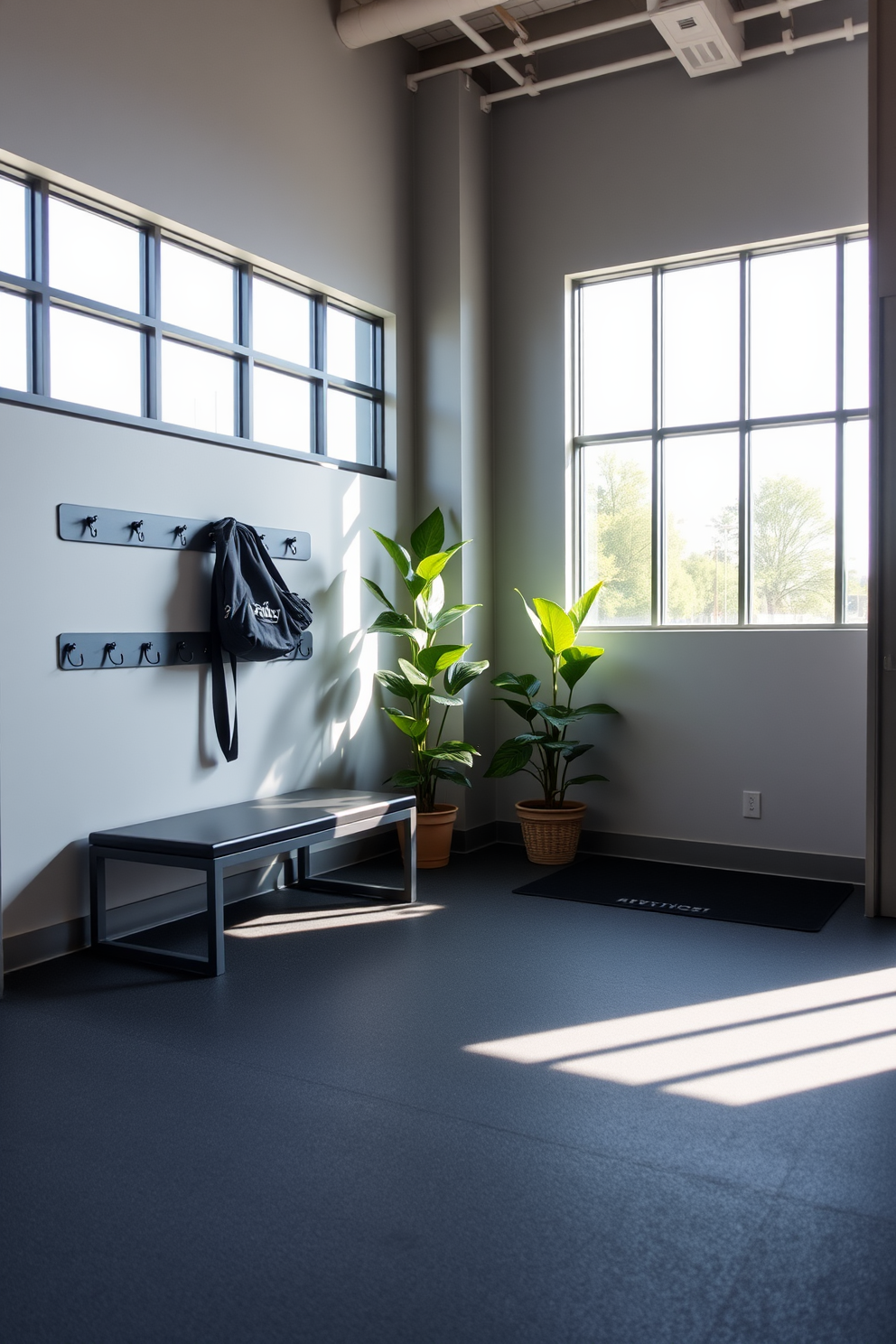 A welcoming entryway to a gym features a spacious layout with natural light streaming in through large windows. The walls are painted in a calming light gray, complemented by a sleek bench for changing shoes and a set of hooks for gym bags. The flooring is a durable rubber material in a dark color, providing both style and functionality. Potted plants are placed near the entrance, adding a touch of greenery and freshness to the space.