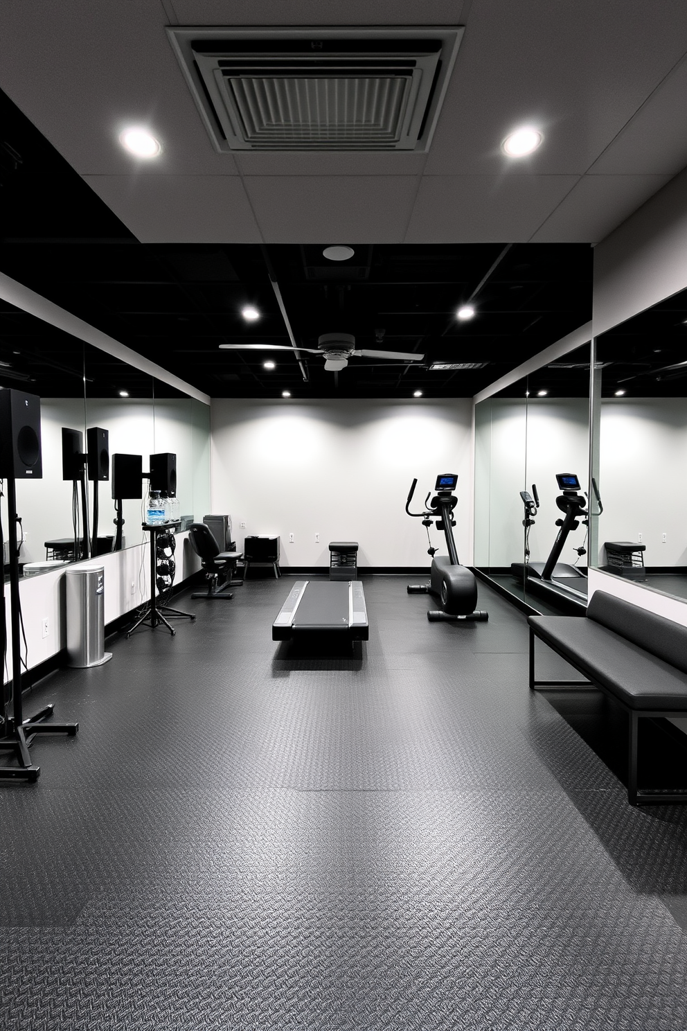 A modern basement gym featuring sleek black rubber flooring and bright LED lighting. The space is equipped with a high-quality sound system to keep the energy up during workouts, along with a variety of exercise machines including a treadmill and a weight bench. On one wall, large mirrors reflect the space, creating an illusion of openness. To add a touch of comfort, a small seating area with a stylish bench and a water cooler is included for hydration breaks.