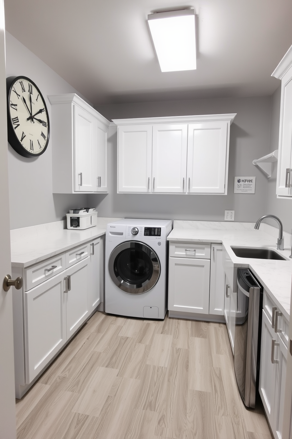 A spacious basement laundry room featuring a large, functional clock mounted on the wall for easy time management. The room is equipped with a modern washer and dryer set, surrounded by ample countertop space for folding clothes. Bright white cabinetry provides storage solutions, while a deep sink is positioned for convenience. The walls are painted in a soft gray, and the floor is covered with durable vinyl planks for easy maintenance.