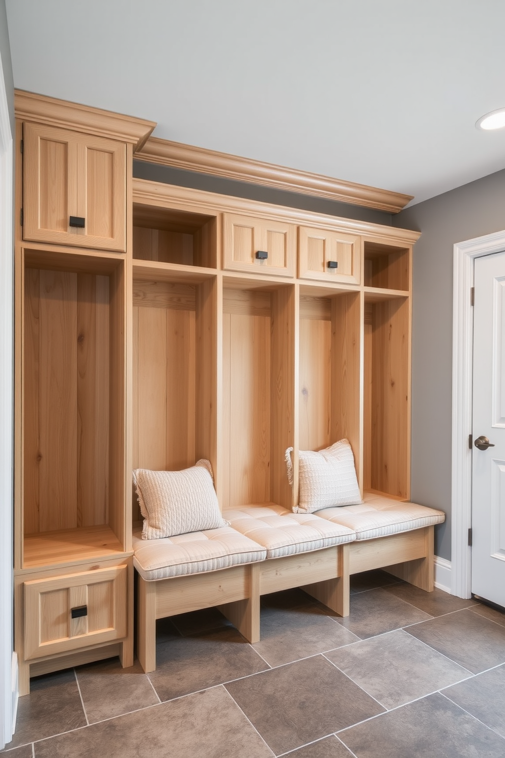 A spacious mudroom featuring built-in cubbies designed for organized storage. The cubbies are crafted from light wood with a natural finish, providing a warm and inviting atmosphere. The walls are painted in a soft gray, complementing the durable tile flooring. A bench is situated beneath the cubbies, adorned with plush cushions for added comfort.