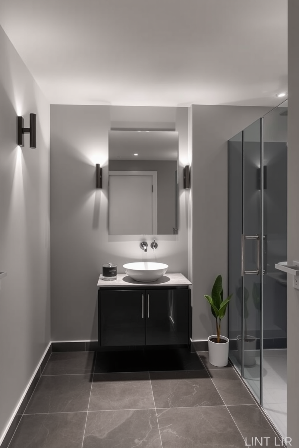 A modern basement washroom featuring wall-mounted lighting that illuminates the space effectively while saving floor area. The walls are painted in a light gray tone, and the flooring consists of sleek porcelain tiles in a dark shade. A compact vanity with a vessel sink sits beneath a large mirror, reflecting the stylish wall sconces on either side. A minimalist shower area with glass doors is situated at the far end, complemented by a small potted plant for a touch of greenery.