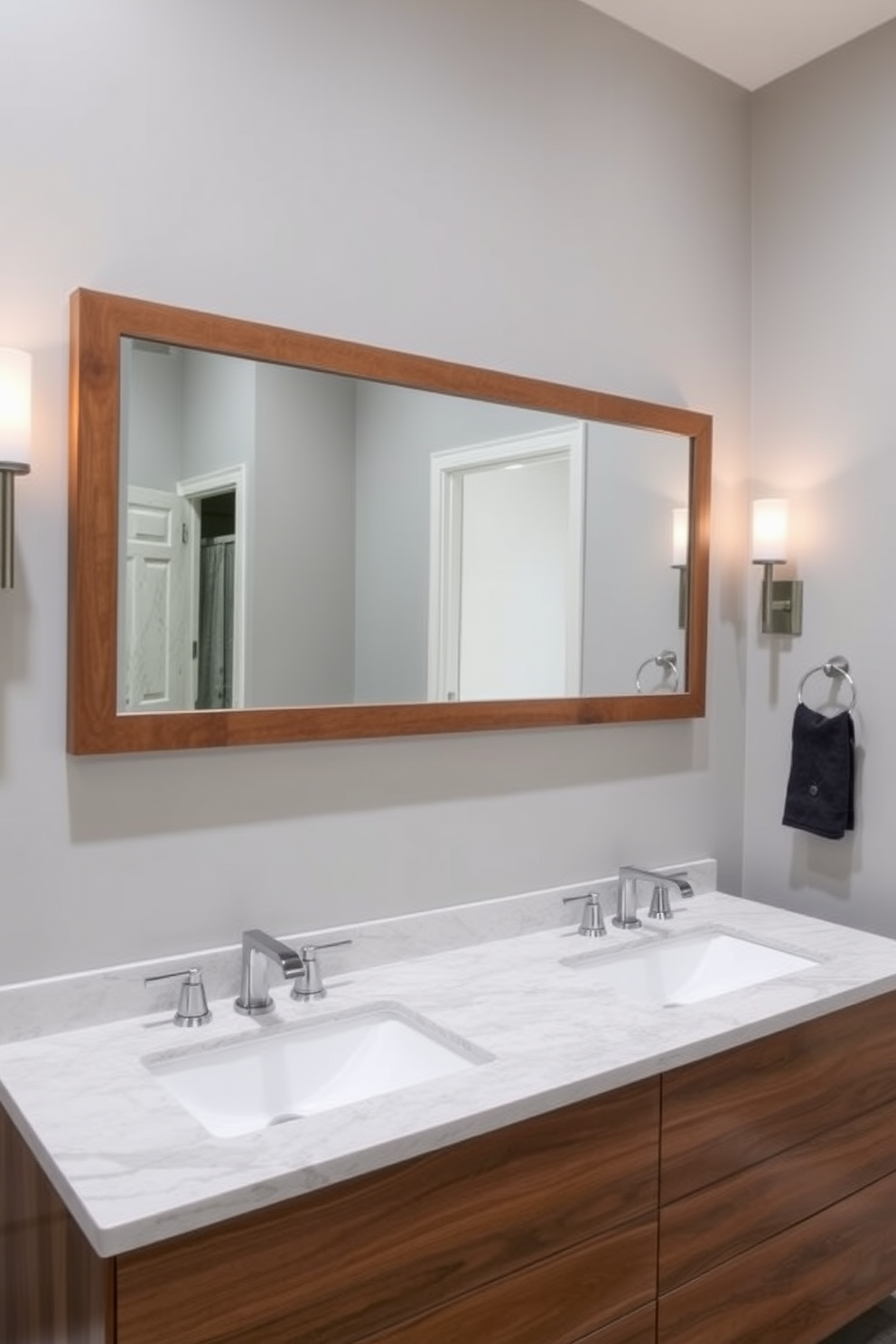 A stylish bathroom featuring dual sinks designed for shared spaces. The sinks are set within a sleek wooden vanity topped with a polished quartz surface, complemented by elegant wall sconces on either side. The walls are adorned with a soft gray hue, creating a calming atmosphere. A large framed mirror stretches above the sinks, reflecting the warm light from the fixtures.