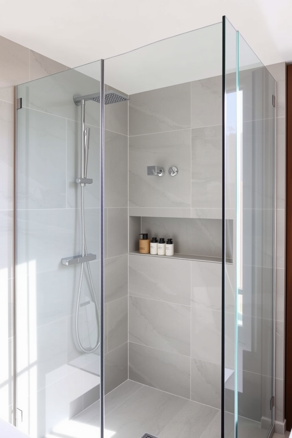 A modern bathroom features wall-mounted shower fixtures that create a sleek and minimalist aesthetic. The shower area is enclosed with clear glass panels, allowing natural light to illuminate the space. The walls are adorned with large format tiles in a soft gray hue, enhancing the contemporary feel. A built-in niche holds stylish toiletries, while a rainfall showerhead adds a touch of luxury to the experience.