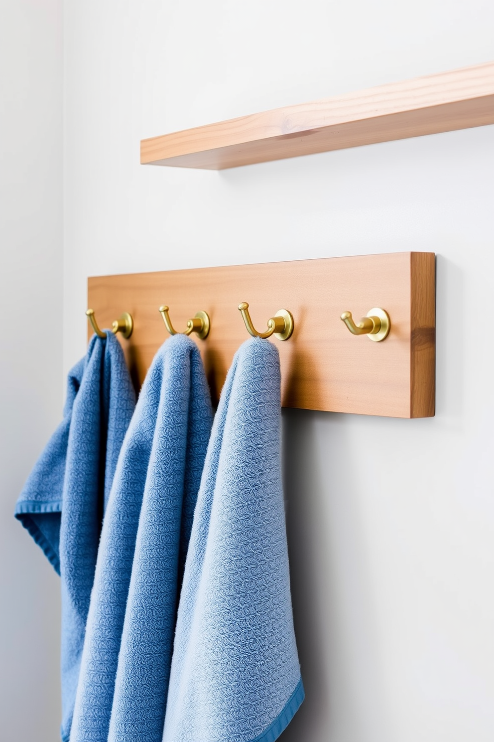 A stylish bathroom featuring decorative hooks for towel display. The hooks are made of brushed brass and are mounted on a wooden board that complements the cabinetry. Soft, fluffy towels in varying shades of blue are elegantly draped over the hooks. The background features a serene color palette with light gray walls and a natural wood accent shelf.