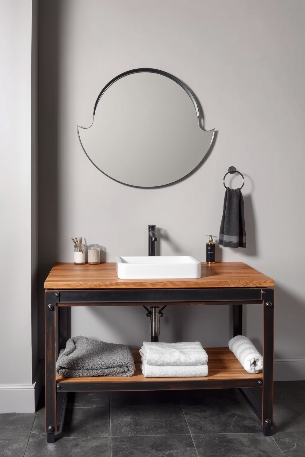 An industrial style bathroom vanity featuring a robust metal frame with exposed hardware. The countertop is made of reclaimed wood, creating a warm contrast with the sleek metal accents. Above the vanity, a large round mirror with a black metal rim reflects the unique design. The walls are painted in a soft gray, and the floor is adorned with dark concrete tiles, enhancing the industrial aesthetic.