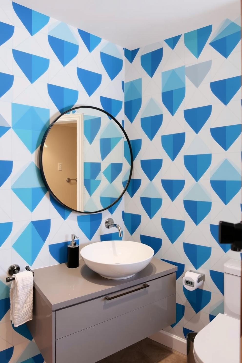 A contemporary bathroom featuring bold geometric shapes that create a striking visual appeal. The wallpaper showcases a vibrant pattern of interlocking triangles in shades of blue and white, enhancing the modern aesthetic of the space. The room is complemented by sleek fixtures and minimalist accessories that accentuate the wallpaper design. A large round mirror with a thin black frame hangs above a floating vanity, adding to the clean lines and sophisticated look of the bathroom.