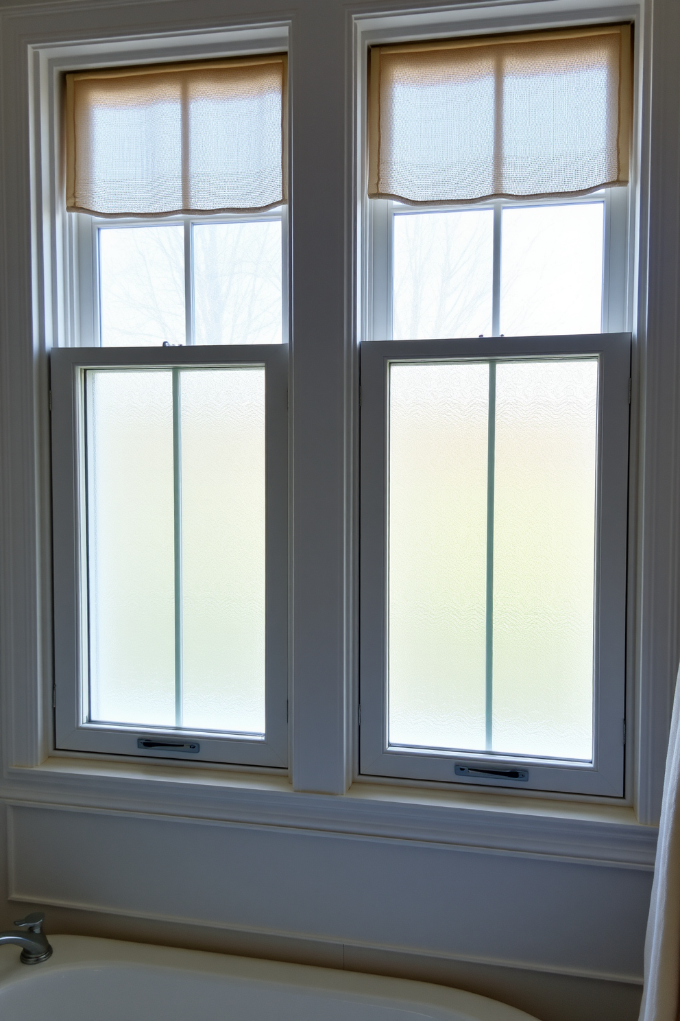 Double hung windows elegantly frame the view, allowing for optimal ventilation and natural light. The design features classic wooden frames painted in a soft white, enhancing the overall aesthetic of the bathroom. Frosted glass panes provide privacy while still inviting sunlight to filter through. Decorative window treatments in a light fabric complement the serene color palette of the space.