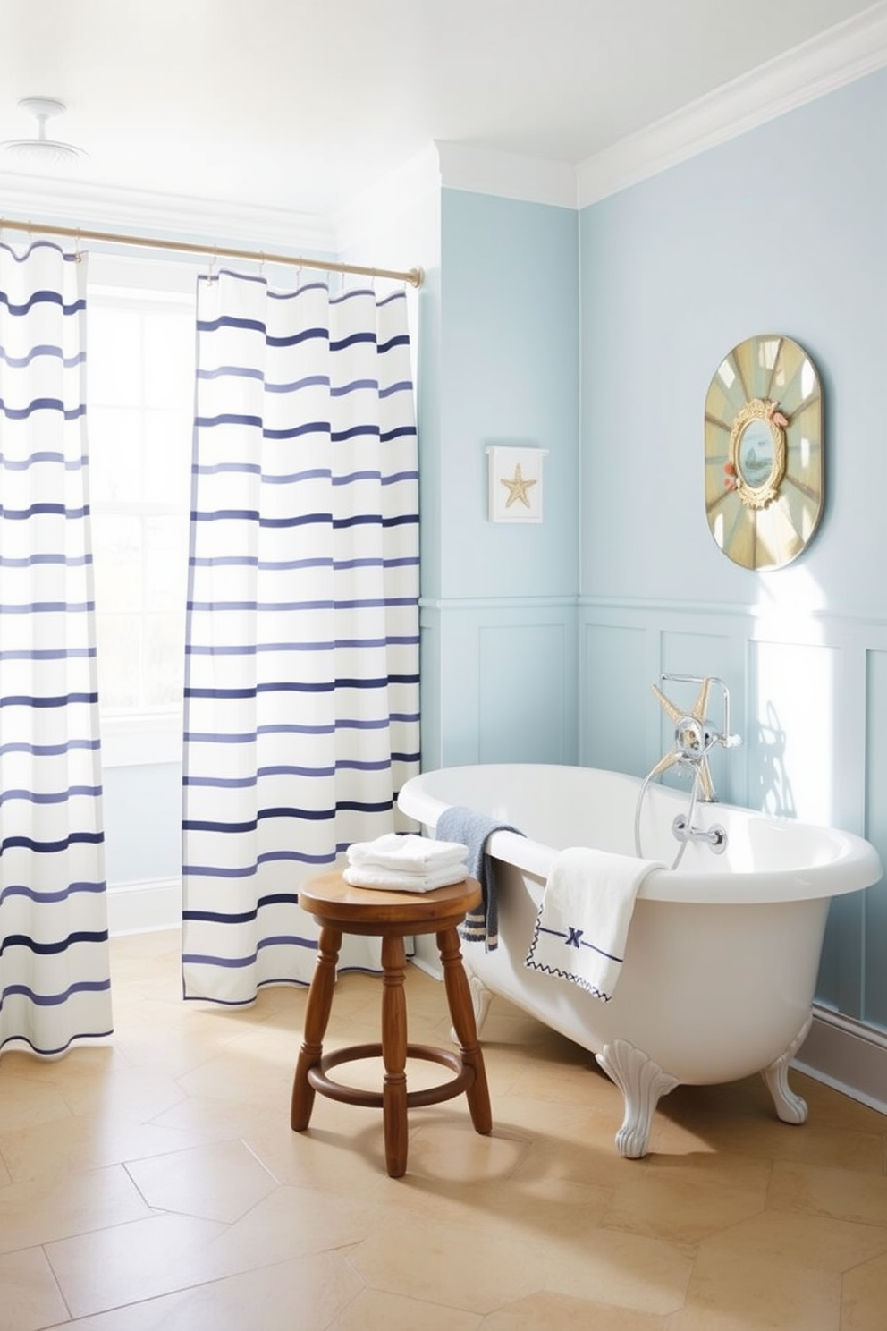 A bright and airy beach bathroom featuring nautical stripes on the shower curtains. The walls are painted in a soft blue hue, complementing the sandy beige tiles on the floor. A vintage wooden stool sits beside a freestanding tub, adorned with sea-themed decor. Natural light pours in through a large window, enhancing the relaxed coastal vibe of the space.