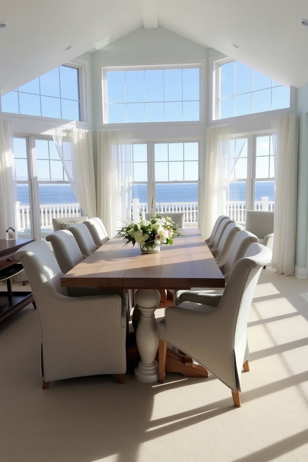 A bright and airy dining room with large windows that let in abundant natural light. The space features a long wooden dining table surrounded by comfortable upholstered chairs in soft coastal colors. Light drapes frame the windows, fluttering gently in the breeze. A centerpiece of fresh flowers adds a touch of nature, complementing the beach-inspired decor throughout the room.