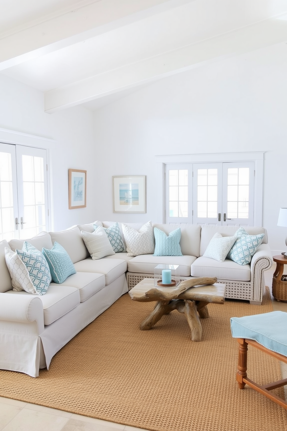 A bright and airy beach living room filled with natural light. The walls are painted in a soft white, and the furniture features a mix of light blue and sandy beige tones. A large sectional sofa is adorned with various textured throw pillows in shades of ocean blue. A woven jute rug anchors the space, while a driftwood coffee table adds a rustic touch.