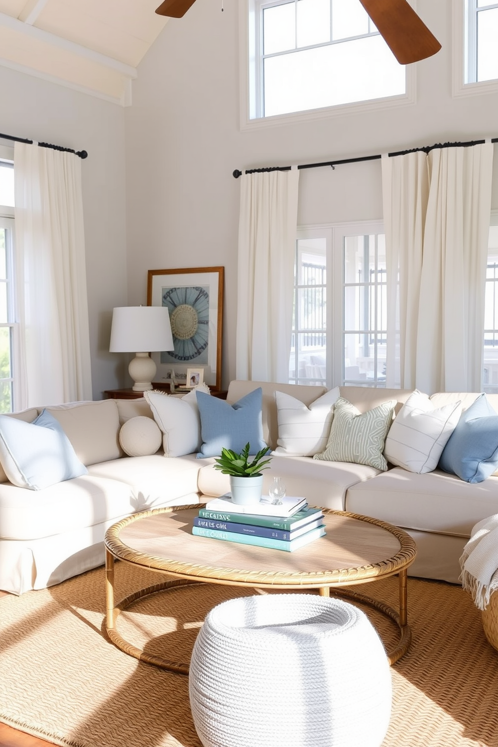 A cozy beach living room filled with layered textiles that enhance comfort and style. Soft white and blue throw pillows are scattered across a plush beige sofa, while a woven area rug anchors the space. Natural light floods the room through large windows adorned with sheer curtains that flutter gently in the breeze. A rattan coffee table sits in the center, topped with a stack of beach-themed books and a small potted plant.