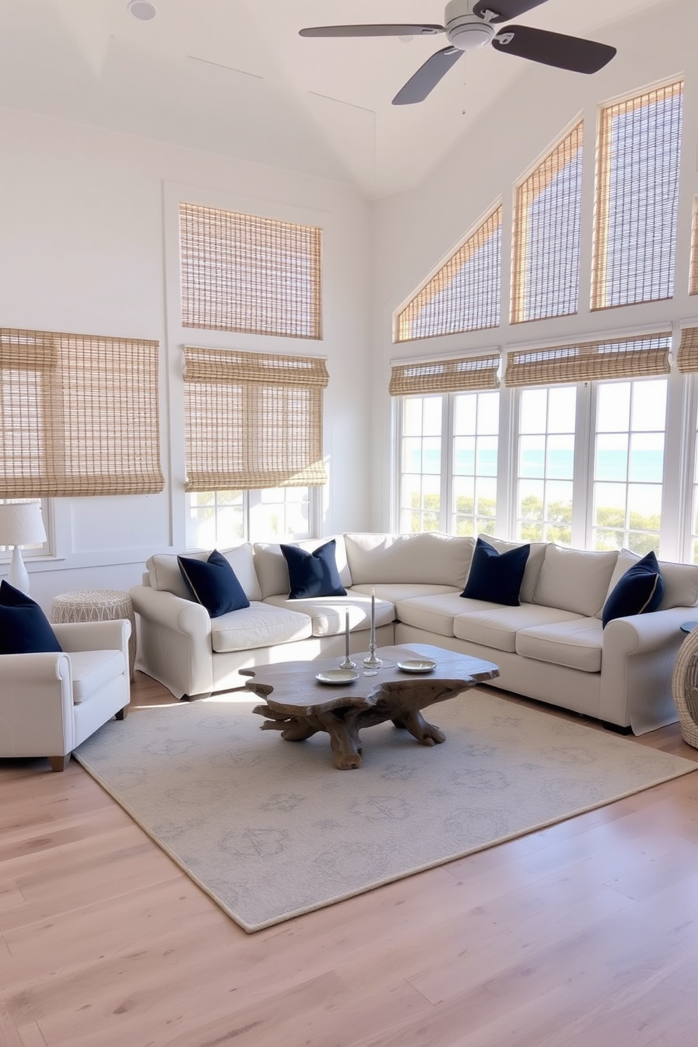 A serene beach living room with soft white walls and light hardwood flooring. Large windows are adorned with bamboo shades that gently filter natural light, creating a warm and inviting atmosphere. The space features a plush sectional sofa in a light beige fabric, accented with navy blue throw pillows. A large area rug with a subtle coastal pattern anchors the seating area, while a driftwood coffee table adds a touch of rustic charm.