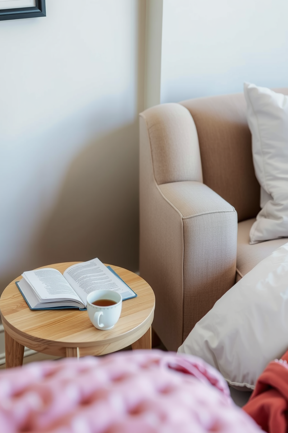 A cozy bedroom reading nook features a small side table made of light wood, perfectly sized for holding a book and a cup of tea. A plush armchair upholstered in soft fabric sits beside the table, inviting relaxation and comfort.