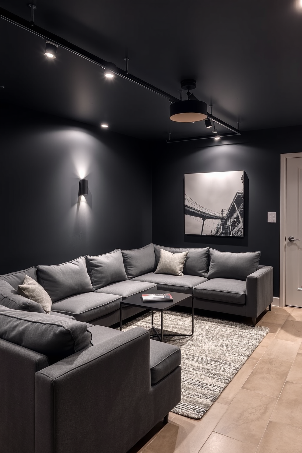 A stylish basement space featuring layered lighting with sleek black fixtures. The walls are painted in a deep charcoal color, and the floor is finished with polished concrete for a modern look. In one corner, a cozy seating area is created with a plush sectional sofa in a rich gray fabric. A contemporary coffee table sits atop a textured area rug, adding warmth to the space.