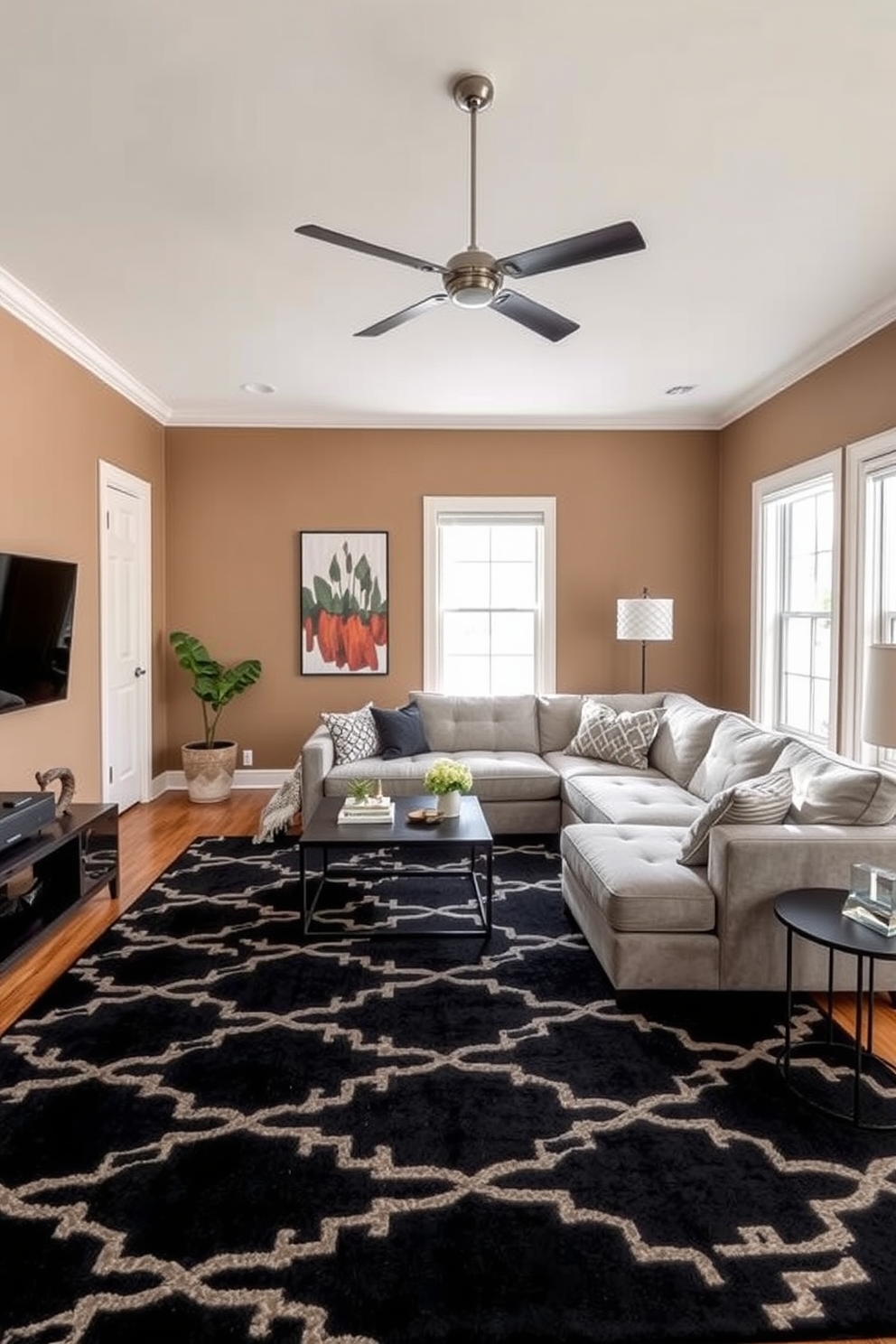 A stylish family room featuring a black area rug with geometric patterns anchoring the space. The walls are painted in a warm taupe color, complemented by a large sectional sofa in a light gray fabric, creating a cozy and inviting atmosphere.