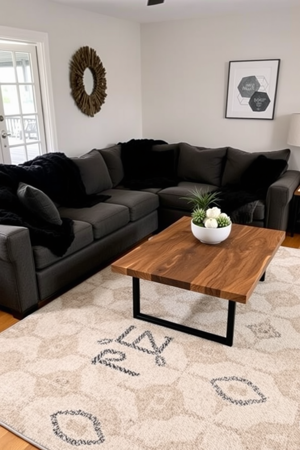 A cozy family room featuring layered textures with plush black throws draped over a deep gray sectional sofa. The space is accented by a large area rug with a subtle geometric pattern, and a coffee table made of reclaimed wood sits at the center.