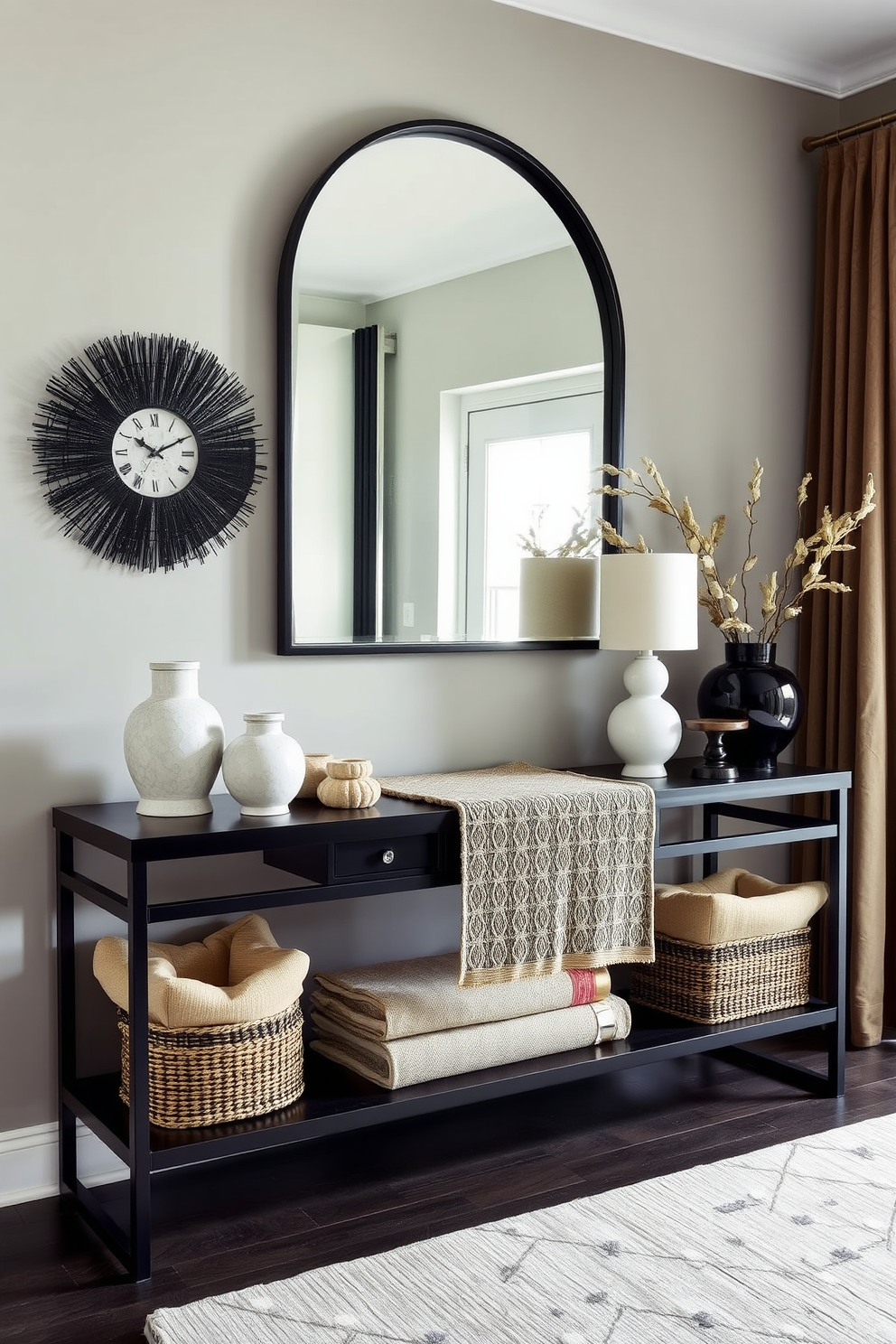 Layered black and neutral textiles create a warm and inviting atmosphere in the foyer. A sleek console table in a dark finish is adorned with a textured runner and decorative objects in varying shades of beige and cream. The walls are painted in a soft gray, complementing the rich black accents throughout the space. A statement mirror with a bold black frame hangs above the console, reflecting the natural light that filters in through a nearby window.