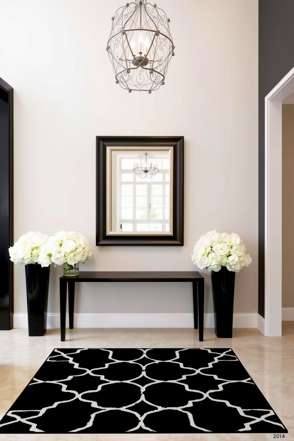 A sophisticated black and cream foyer featuring a sleek black console table against the wall. Above the table, an elegant cream-colored mirror with intricate detailing reflects the soft light from a stylish chandelier above. The floor is adorned with a striking black and cream geometric patterned rug that adds depth to the space. Flanking the console table are tall black vases filled with lush white flowers, creating a stunning contrast and inviting ambiance.