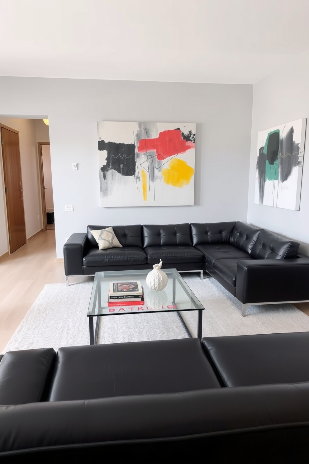 Modern minimalist design with clean lines. The space features a sleek black leather sectional sofa paired with a glass coffee table, creating an open and airy atmosphere. The walls are painted in a soft gray tone, enhancing the overall elegance. A large abstract painting with bold colors serves as a focal point, while subtle lighting highlights the room's features.