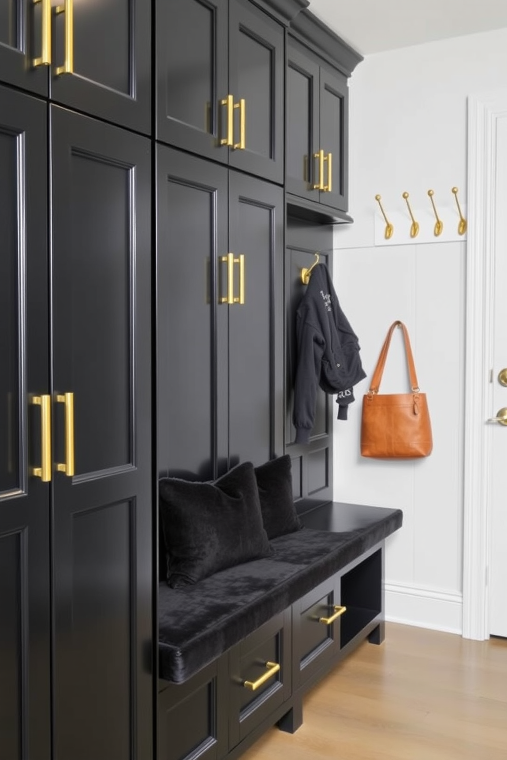 A stylish mudroom featuring black cabinetry with gold hardware. The space includes a bench with plush black cushions and a wall of hooks adorned with gold accents.