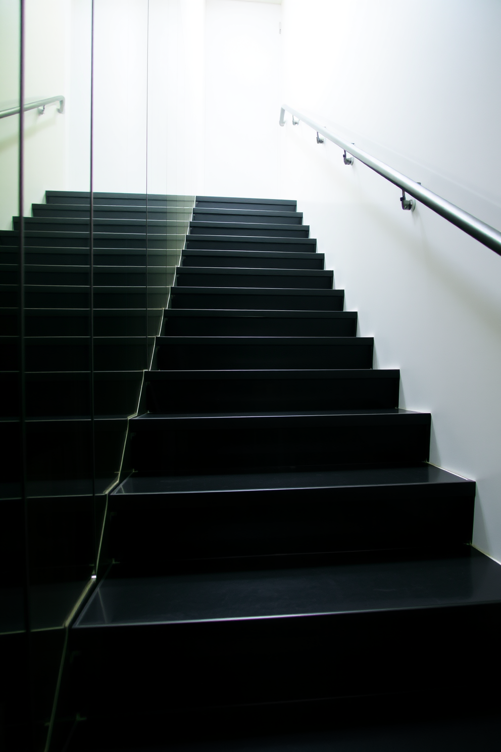 A sleek black staircase ascends gracefully, featuring a minimalist design that emphasizes clean lines and modern aesthetics. The mirrored wall alongside the staircase reflects the surrounding space, creating an illusion of depth and elegance.