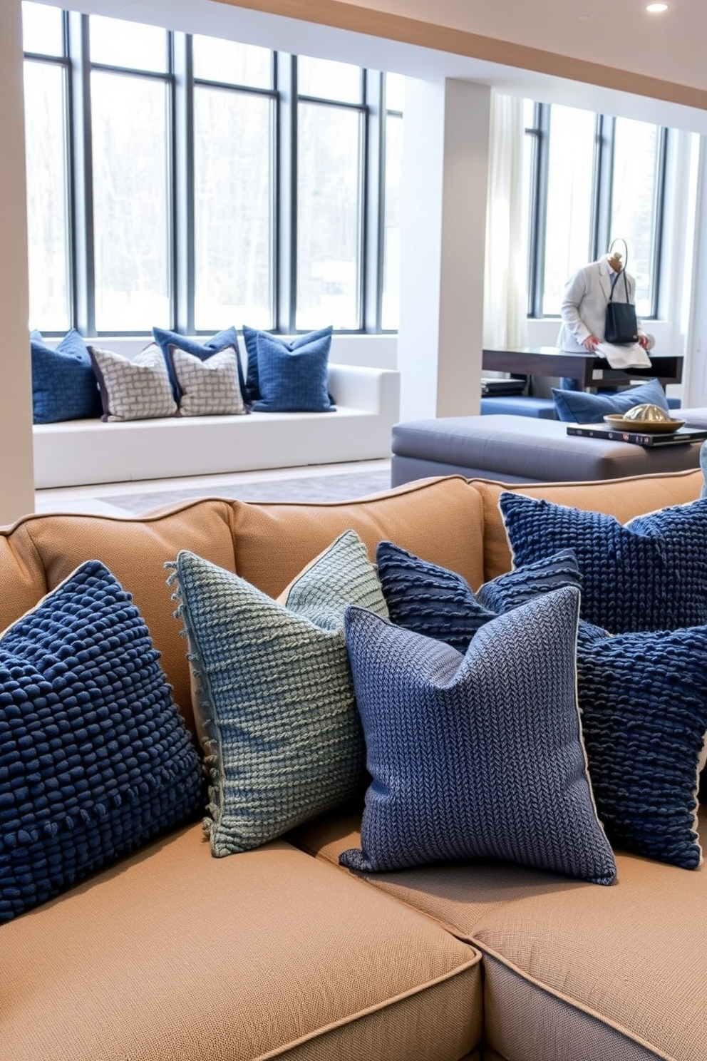 Textured blue throw pillows arranged on a plush sectional sofa create a cozy and inviting atmosphere. The pillows vary in shades of blue and patterns, adding depth and visual interest to the space. The basement features a modern design with sleek lines and an open layout. Large windows allow natural light to flood in, illuminating the stylish furnishings and decor.