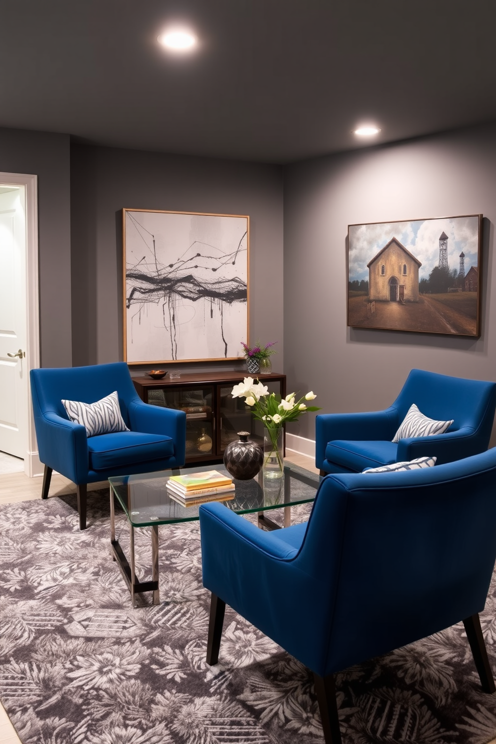 A stylish basement retreat featuring blue accent chairs with modern lines positioned around a sleek glass coffee table. The walls are painted in a cool gray tone, complemented by plush area rugs and contemporary artwork that enhances the inviting atmosphere.