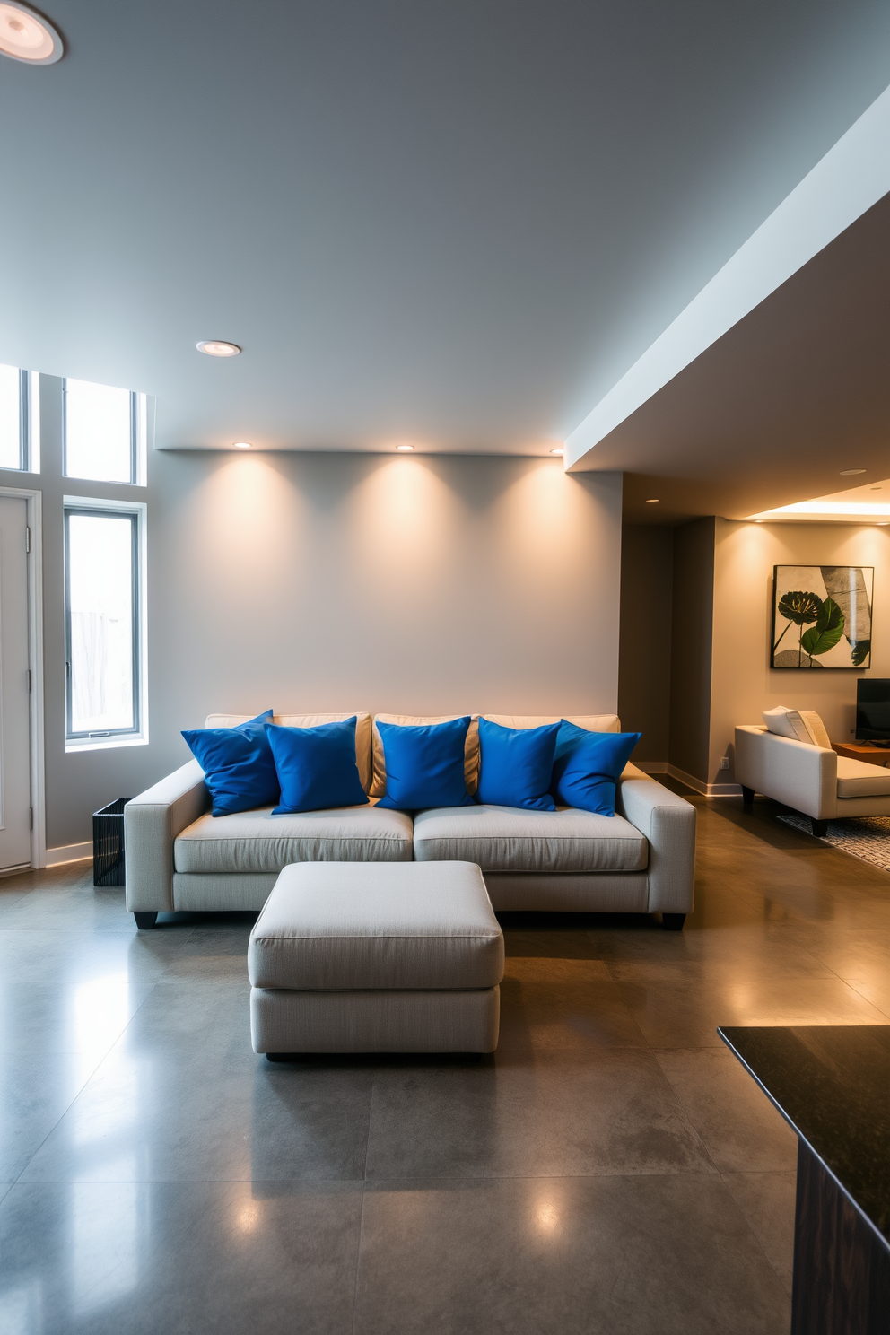 Bright blue cushions are arranged on a neutral-colored sofa, creating a striking contrast that enhances the cozy atmosphere. The walls are painted in a soft gray, and ambient lighting casts a warm glow throughout the space. The basement features a sleek design with polished concrete floors and modern furnishings. Large windows allow natural light to flood in, making the area inviting and functional for relaxation or entertainment.