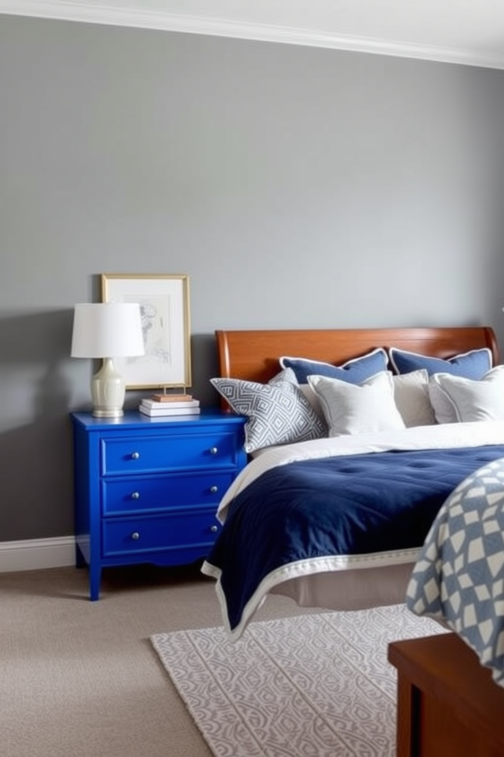 A cobalt blue dresser serves as the focal point of the room, adding a vibrant modern twist to the space. The walls are painted in a soft gray, creating a calming contrast that enhances the boldness of the dresser. Plush bedding in varying shades of blue and white complements the dresser, creating a cohesive color palette. Decorative pillows with geometric patterns add texture and interest to the overall bedroom design.