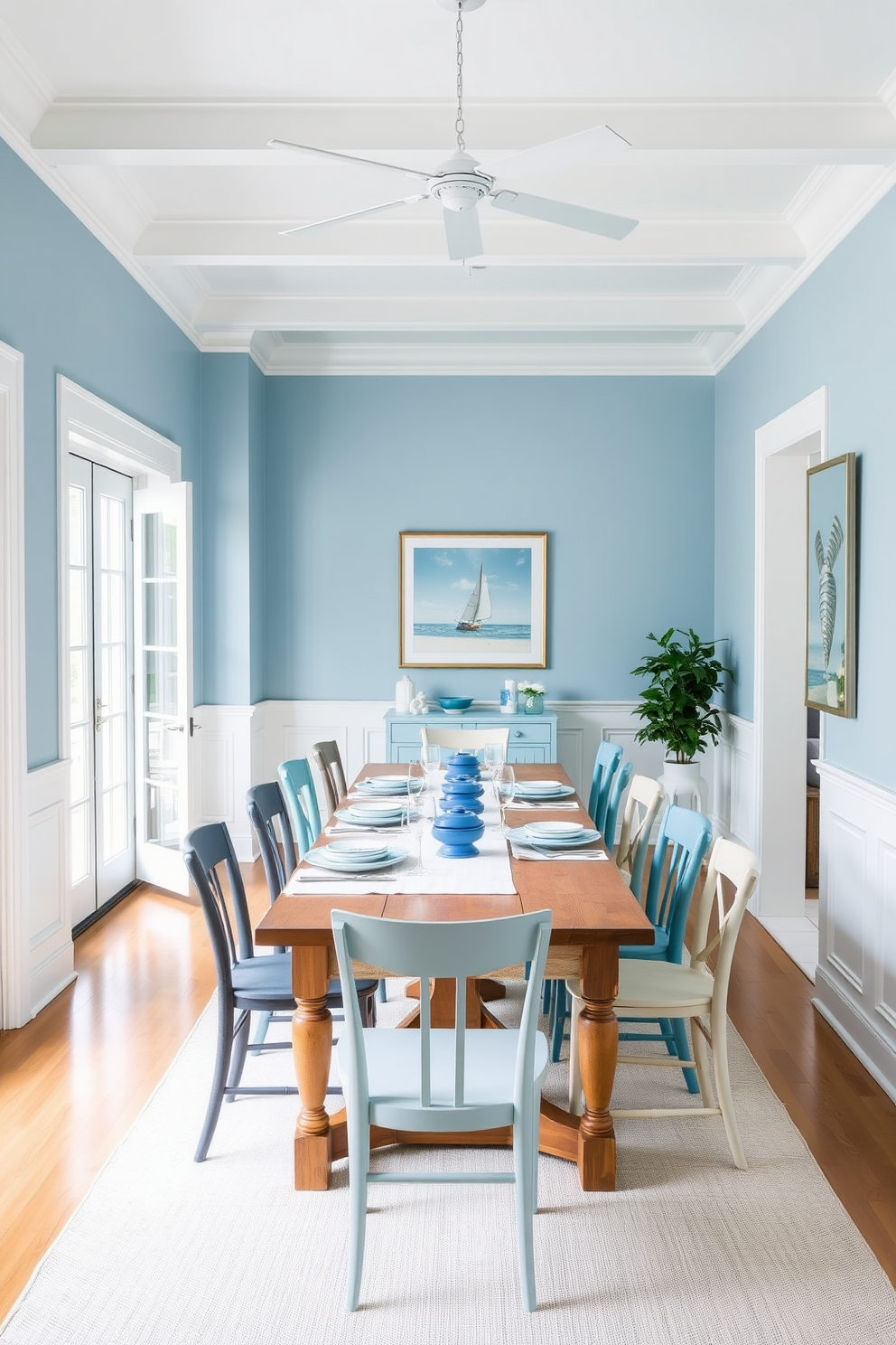 A bright and airy dining room featuring coastal blue and white decor. The walls are painted in a soft blue hue, complemented by white wainscoting and a large window that lets in natural light. A long wooden dining table is set in the center, adorned with a white tablecloth and blue dinnerware. Surrounding the table are mismatched chairs in various shades of blue and white, creating a relaxed and inviting atmosphere.