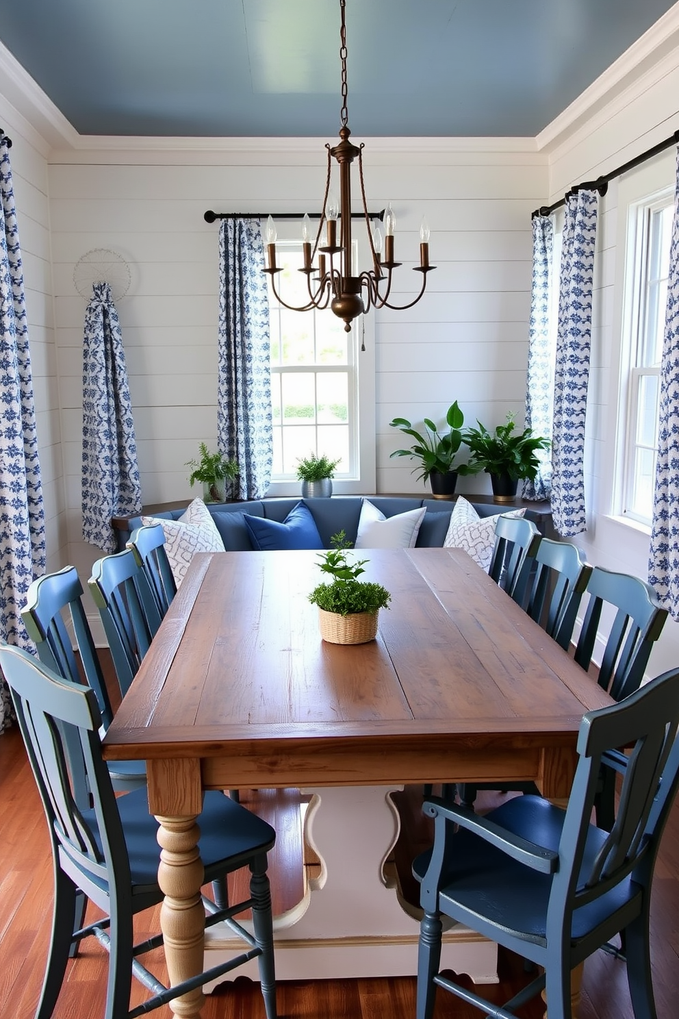 A rustic farmhouse dining room featuring a large wooden table with a distressed finish surrounded by mismatched chairs in various shades of blue. The walls are adorned with shiplap and accentuated by blue and white patterned curtains that frame the windows, allowing natural light to fill the space. A cozy corner nook with a built-in bench upholstered in a soft blue fabric, complemented by throw pillows in varying textures. A vintage chandelier hangs above the table, casting a warm glow over the room, while potted plants add a touch of greenery to the rustic charm.