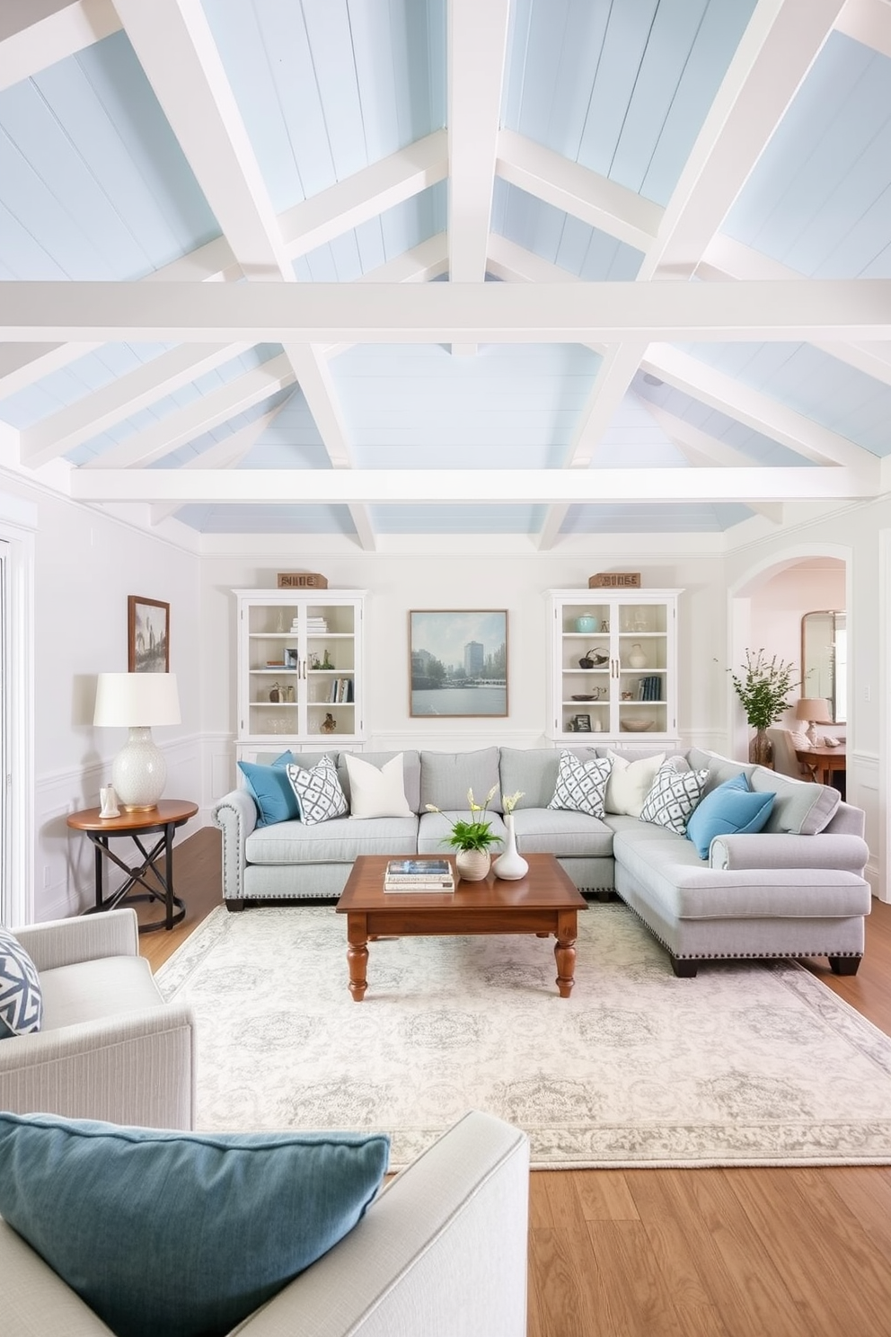 A serene family room featuring a light blue ceiling adorned with white wooden beams. The walls are painted in a soft white, creating a bright and airy atmosphere that complements the ceiling. Cozy seating arrangements include a plush sectional sofa in a light gray fabric paired with accent pillows in various shades of blue. A large area rug with subtle patterns anchors the space, while a wooden coffee table sits at the center, adorned with decorative books and a small plant.