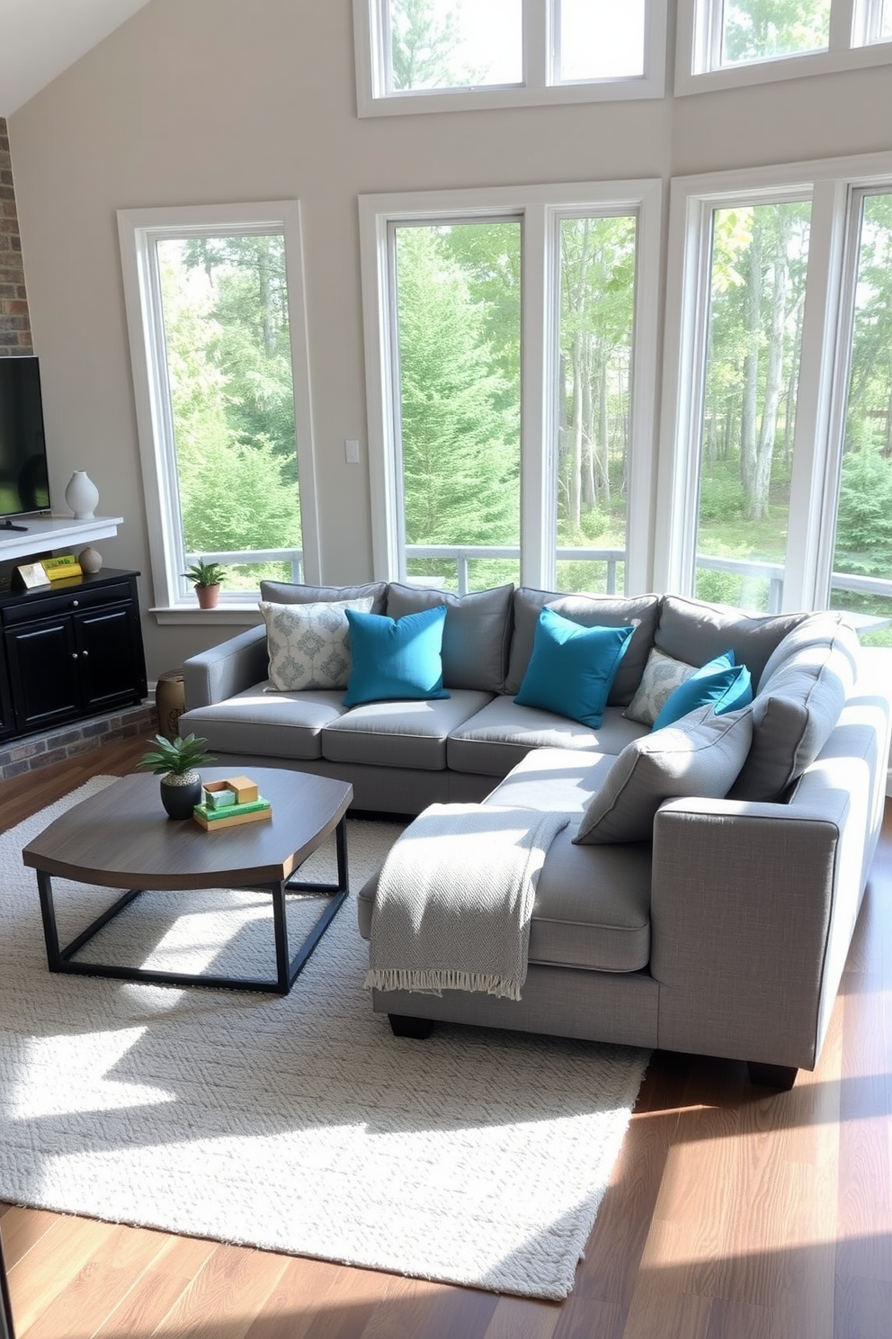 A cozy family room featuring a gray sectional sofa adorned with teal cushions. The space is brightened by large windows allowing natural light to flow in, complemented by a soft area rug underfoot.