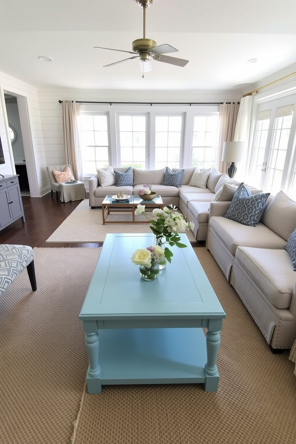 A cozy family room featuring a robin's egg blue coffee table as the centerpiece. Surrounding the table are a plush sectional sofa in neutral tones and a pair of accent chairs with a geometric pattern. The walls are adorned with soft white shiplap, creating a warm and inviting atmosphere. Large windows allow natural light to flood the space, complemented by light sheer curtains.