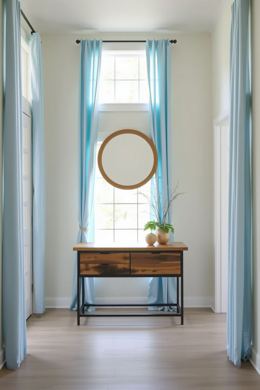 A bright and inviting foyer featuring soft blue curtains that gently frame a large window, allowing natural light to flood the space. The walls are painted in a light neutral tone, complementing the airy feel created by the curtains. In the center of the foyer, a stylish console table made of reclaimed wood adds warmth and character. A round mirror with a simple wooden frame hangs above the table, reflecting the light and enhancing the spacious atmosphere.