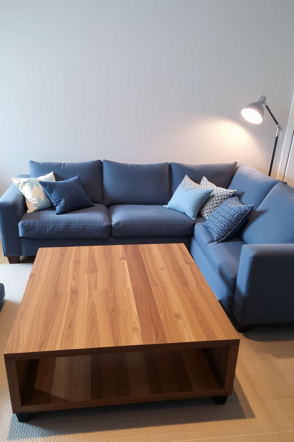 A muted blue sectional sofa is positioned against a light gray wall, creating a cozy and inviting atmosphere. In front of the sofa, a sleek wooden coffee table adds warmth and serves as a focal point in the space. The room features soft lighting from a stylish floor lamp in the corner, enhancing the overall ambiance. Decorative cushions in varying shades of blue and white are scattered across the sectional, adding texture and comfort.