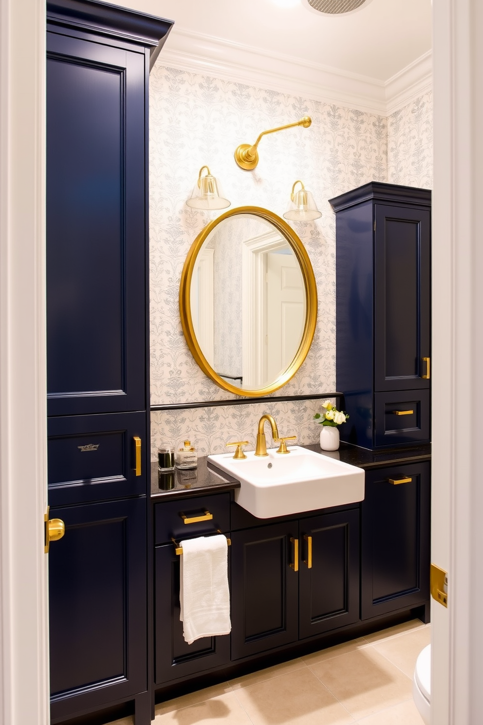 Navy blue cabinets with gold fixtures create a striking contrast in a chic powder room. The walls are adorned with a delicate wallpaper pattern that complements the rich cabinetry. A round mirror with a gold frame hangs above a sleek white sink, enhancing the elegance of the space. Soft lighting fixtures illuminate the room, casting a warm glow on the luxurious finishes.