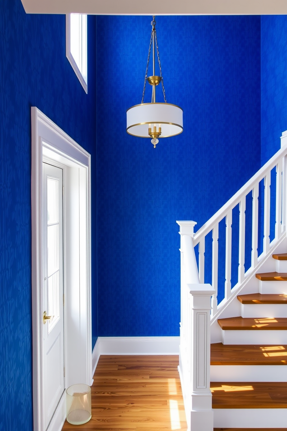 A striking staircase adorned with bold royal blue wallpaper that features a subtle geometric pattern. The wallpaper creates a dramatic focal point, contrasting beautifully with the crisp white banister and wooden steps. The staircase is illuminated by a modern chandelier that adds elegance to the space. Natural light streams in from a nearby window, enhancing the vibrant blue tones and creating a welcoming atmosphere.