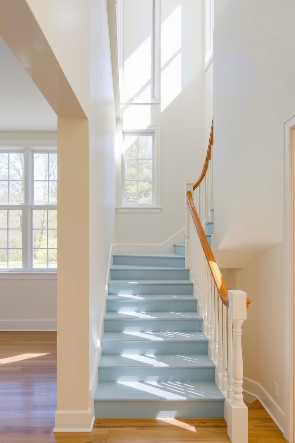 A serene light blue and cream palette creates a calming atmosphere in the space. The walls are painted in a soft cream, while the staircase features light blue risers that complement the overall design. The staircase is elegantly designed with a sleek wooden handrail and white spindles. Natural light floods the area through large windows, enhancing the tranquil feel of the light blue and cream color scheme.