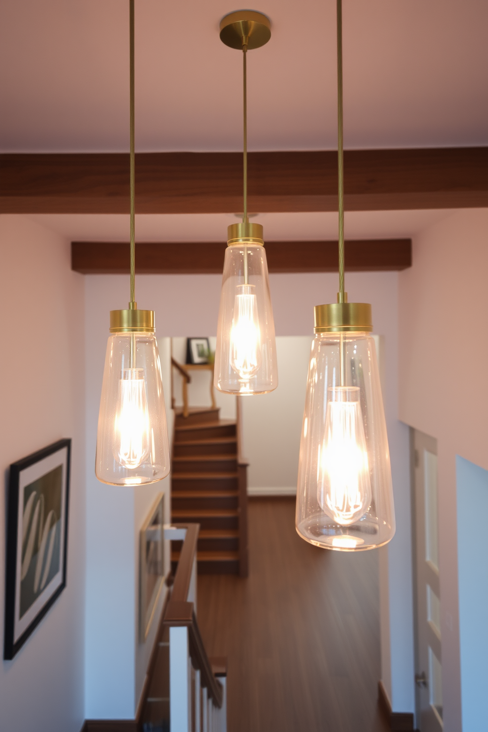 Hanging pendant lights create an elegant ambiance in a spacious entryway. The fixtures are made of glass and brass, casting a warm glow that highlights the architectural details of the space. The closed staircase features a sleek design with wooden steps and a minimalist railing. The walls are adorned with artwork, complementing the overall aesthetic while providing a sense of intimacy.