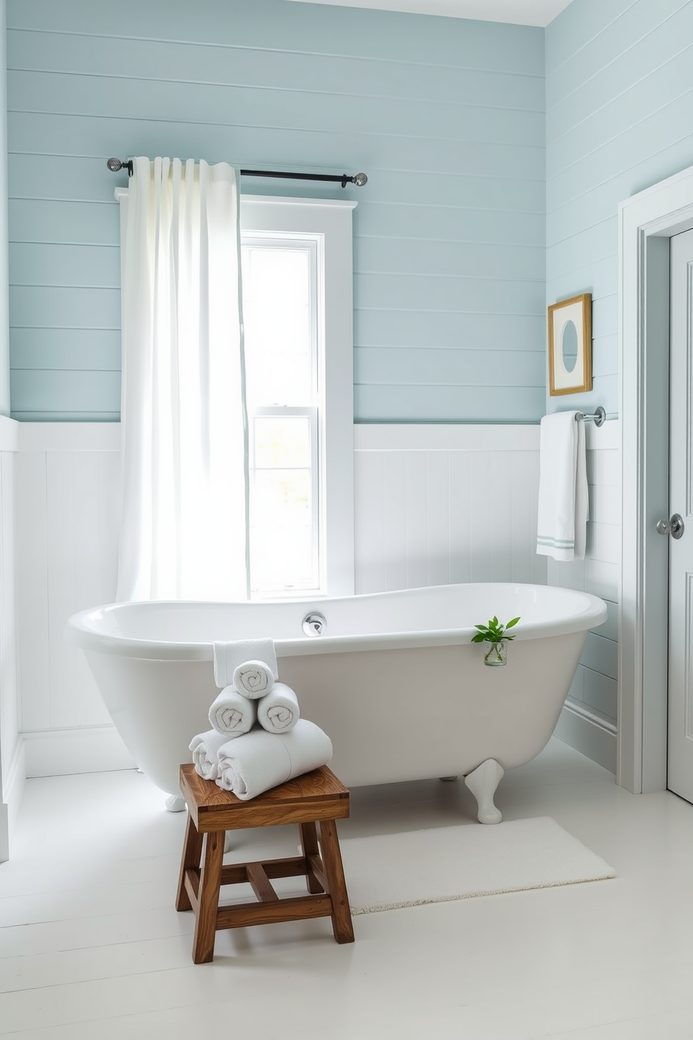 A serene coastal bathroom design featuring a soothing color palette of soft blues and crisp whites. The walls are adorned with shiplap panels painted in a light blue hue, creating a fresh and airy atmosphere. The focal point is a freestanding white bathtub positioned near a window with sheer white curtains. Complementing the bathtub, a rustic wooden stool holds a collection of neatly rolled white towels and a small potted plant for a touch of greenery.