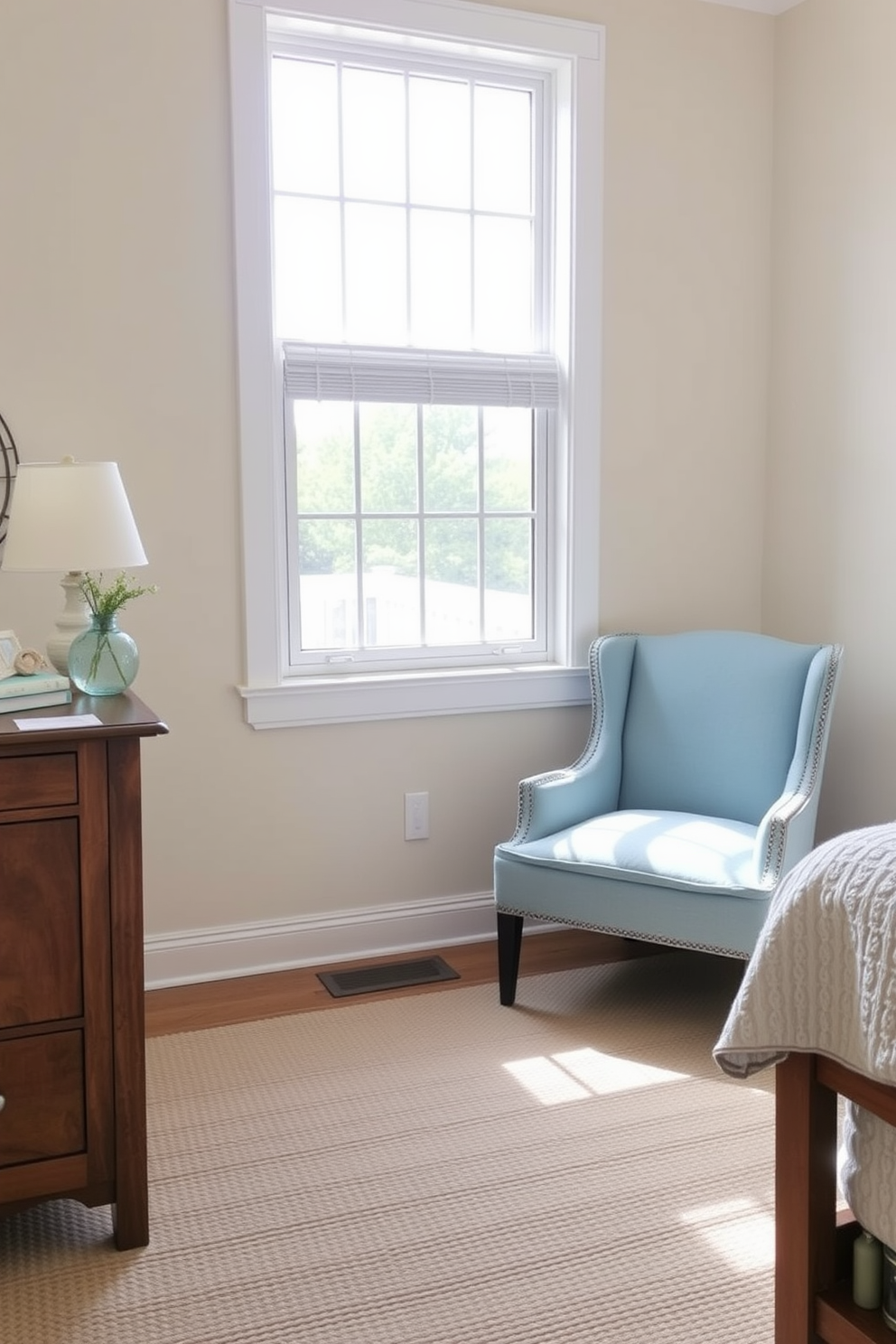 A coastal bedroom featuring a soft blue accent chair positioned near a large window. The room is filled with natural light, and the walls are painted in a light sandy beige, complemented by white shiplap accents.