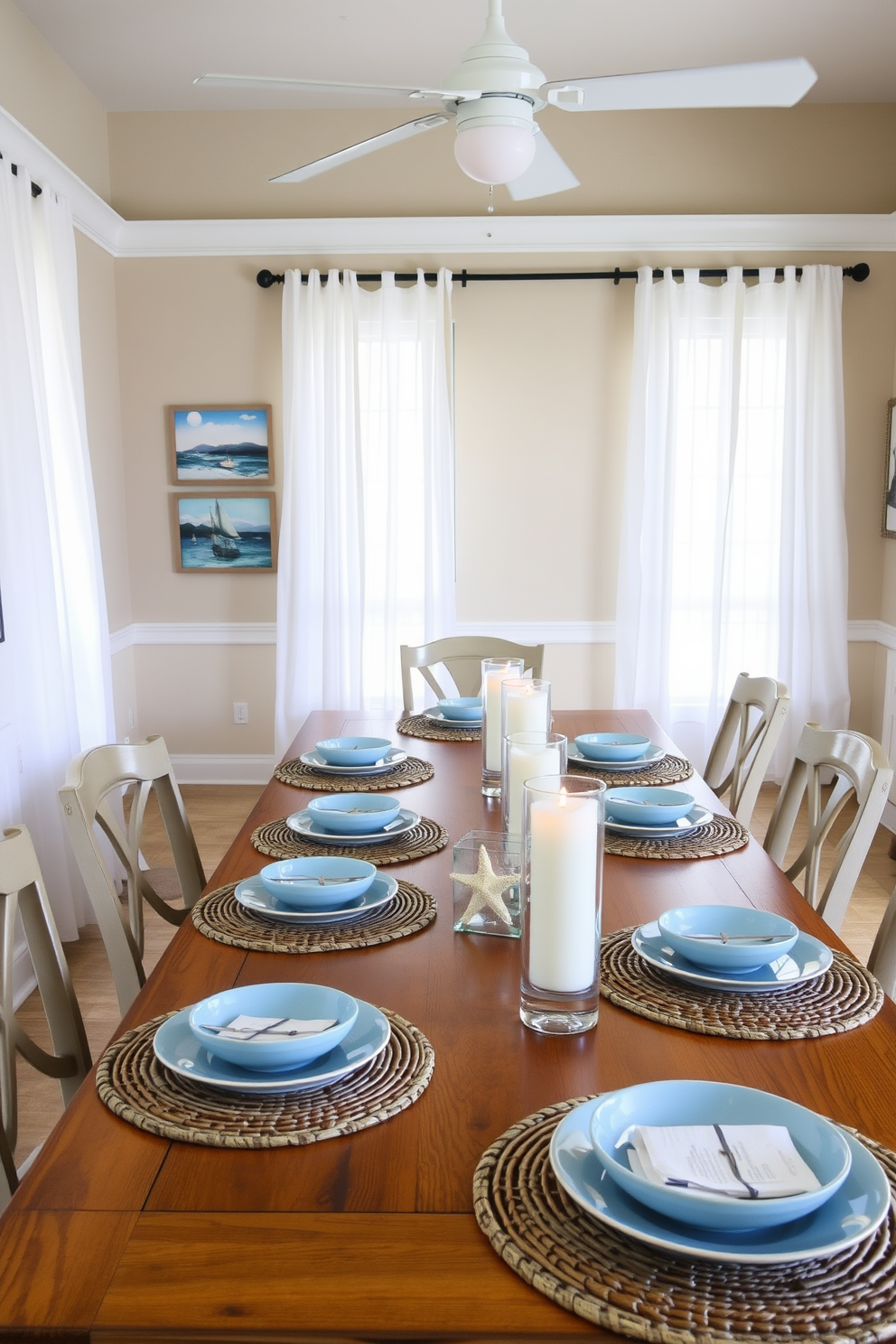 A coastal dining room features a long wooden table set with light blue plates and woven placemats. Starfish accents are placed as centerpieces alongside soft white candles in glass holders. The walls are painted in a sandy beige color, complemented by sheer white curtains that flutter gently in the breeze. Nautical-inspired artwork adorns the walls, bringing a touch of the ocean indoors.