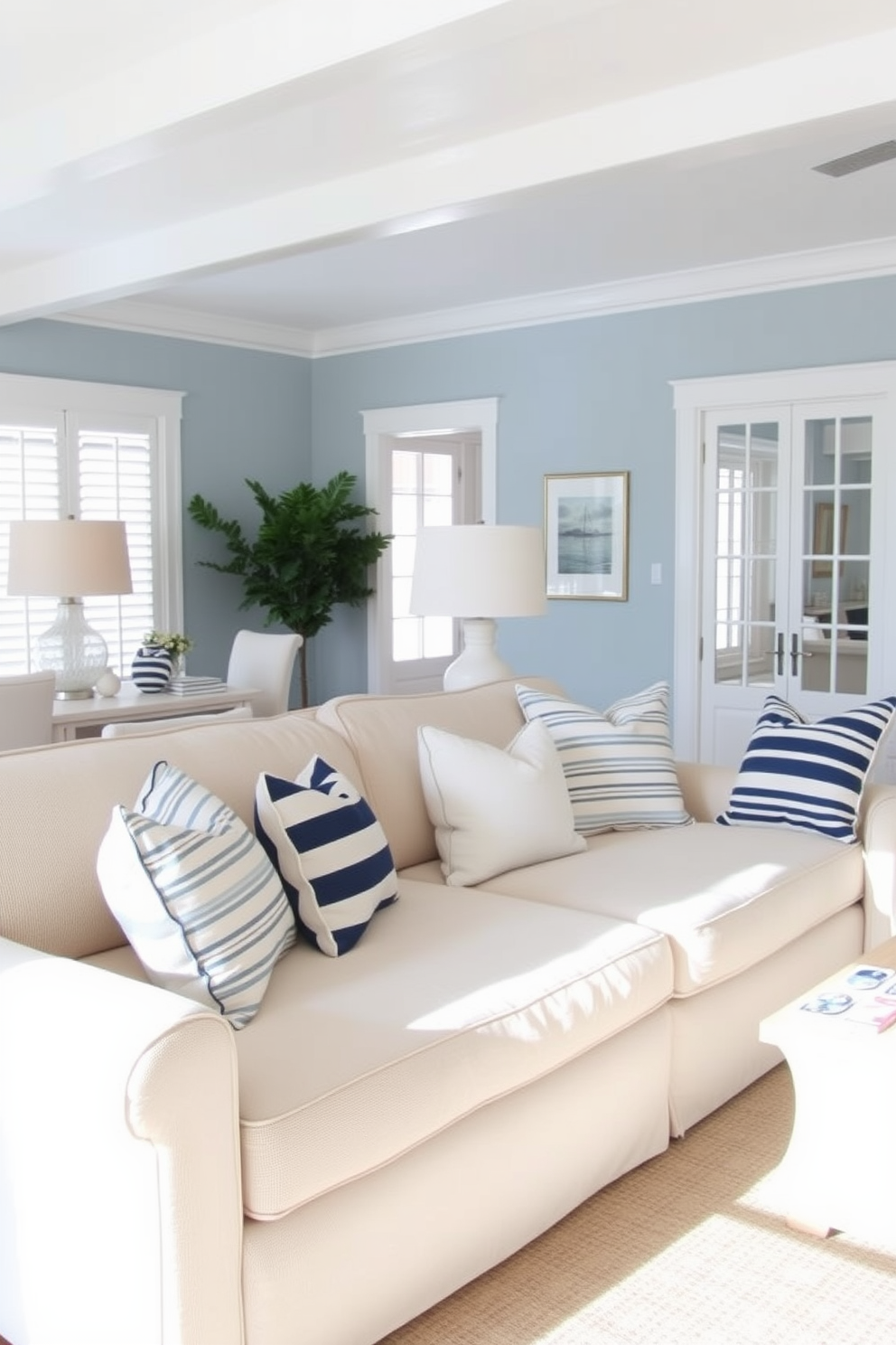 A coastal living room featuring a soft beige sofa adorned with nautical stripes on throw pillows. The room is bright and airy, with large windows allowing natural light to flood in and a subtle blue accent wall that evokes a serene beach vibe.